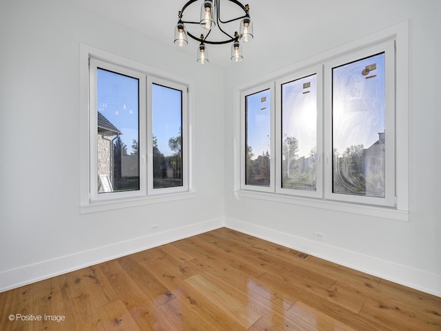 spare room with a chandelier, baseboards, and light wood-style floors