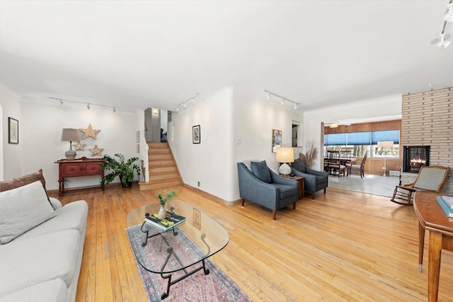 living area with track lighting, hardwood / wood-style flooring, crown molding, a brick fireplace, and stairs