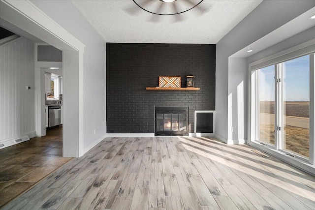 unfurnished living room with a brick fireplace, a textured ceiling, baseboards, and wood finished floors