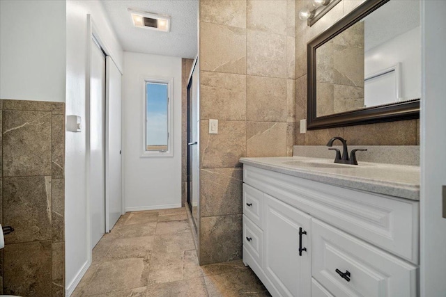 full bathroom featuring tile walls, a shower stall, vanity, and stone tile floors