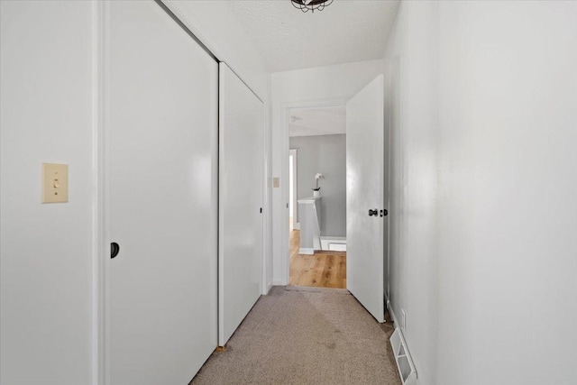 hallway with light carpet, visible vents, and a textured ceiling