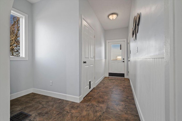 hall with stone finish floor, baseboards, visible vents, and a wealth of natural light