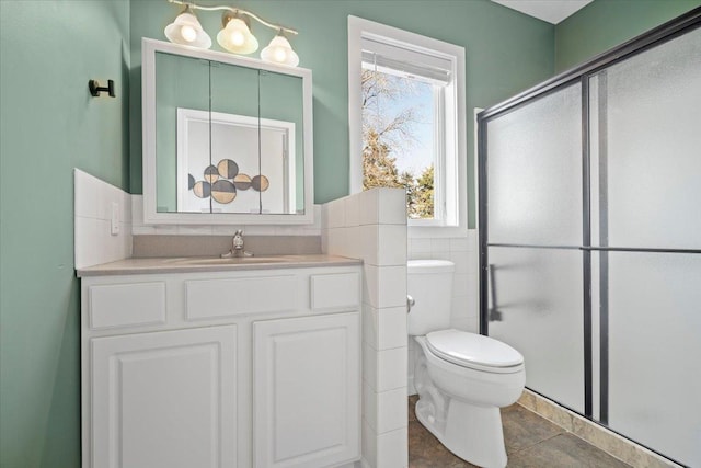 bathroom with vanity, a shower with shower door, wainscoting, tile walls, and toilet