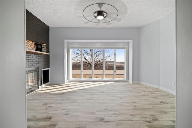 unfurnished living room featuring wood finished floors, a fireplace, baseboards, and a textured ceiling