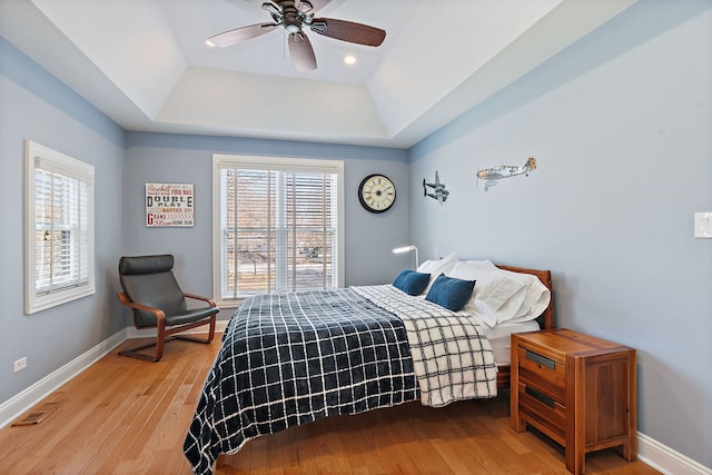 bedroom featuring multiple windows, a raised ceiling, baseboards, and wood finished floors