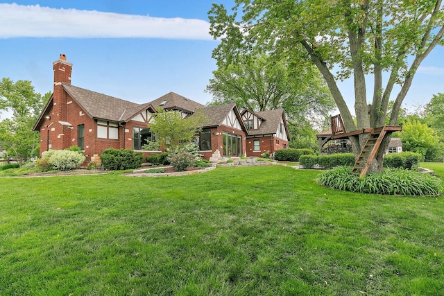 tudor home with brick siding, a chimney, a front yard, and a shingled roof