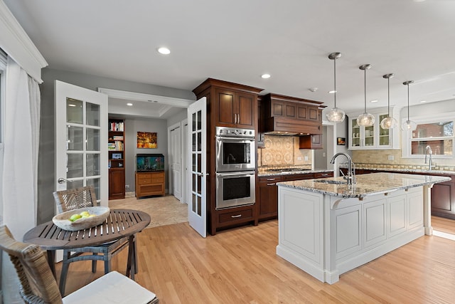 kitchen featuring backsplash, stainless steel appliances, glass insert cabinets, and light wood finished floors