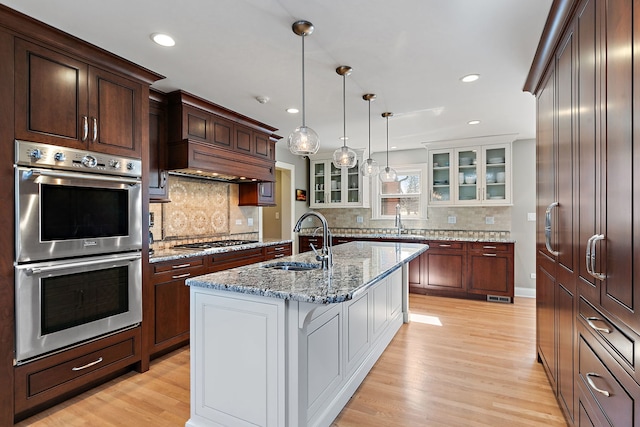 kitchen with a sink, stainless steel appliances, light wood-style floors, and glass insert cabinets