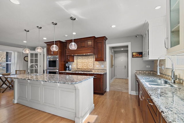 kitchen with a sink, stainless steel appliances, glass insert cabinets, and light wood finished floors