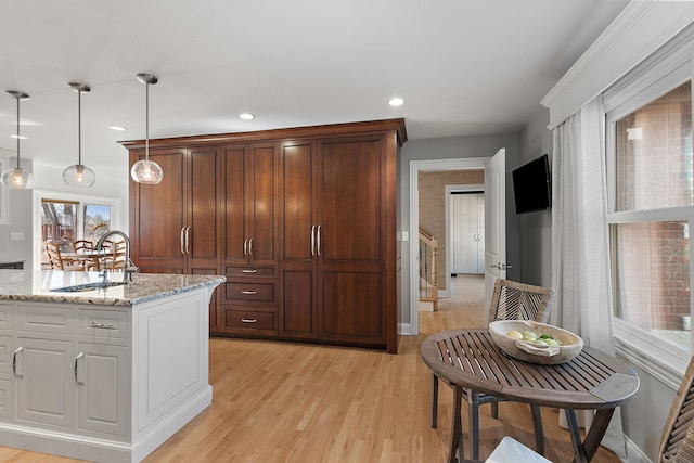 kitchen featuring pendant lighting, a sink, recessed lighting, light wood finished floors, and light stone countertops