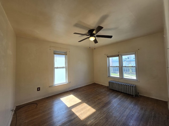 empty room with baseboards, dark wood-type flooring, radiator, and a ceiling fan