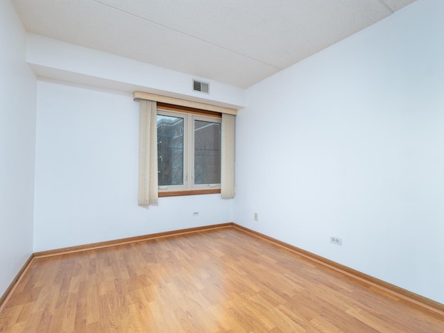 unfurnished room featuring light wood finished floors, visible vents, and baseboards