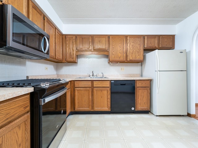 kitchen with a sink, stainless steel microwave, gas range oven, freestanding refrigerator, and dishwasher