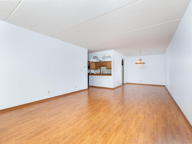 unfurnished living room featuring light wood-type flooring, arched walkways, a textured ceiling, and baseboards