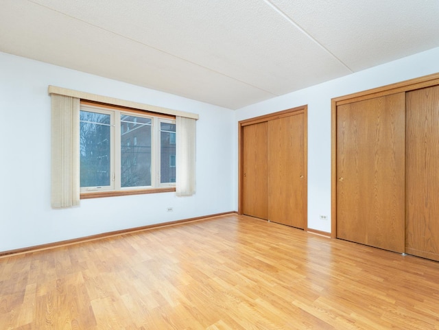 unfurnished bedroom featuring a textured ceiling, baseboards, multiple closets, and wood finished floors