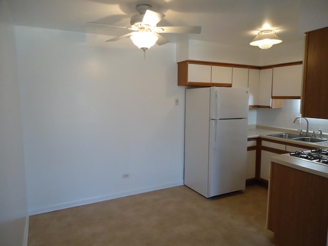 kitchen with baseboards, freestanding refrigerator, a sink, light countertops, and white cabinets