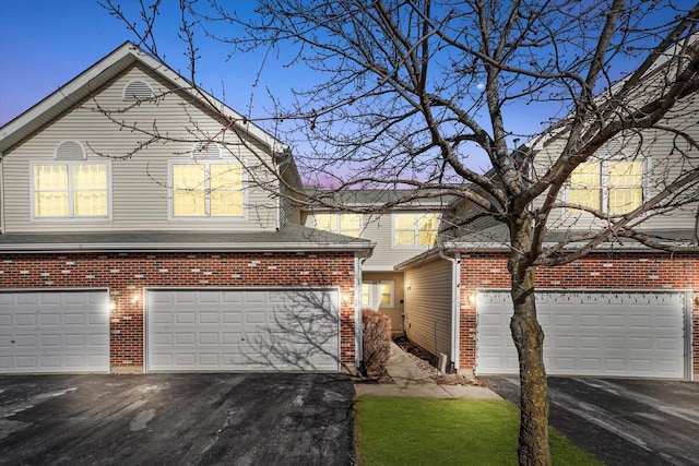 traditional-style home with aphalt driveway, brick siding, a garage, and roof with shingles