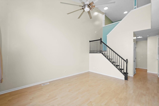 interior space with wood finished floors, a high ceiling, baseboards, ceiling fan, and stairs