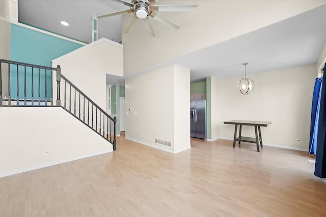 unfurnished living room featuring visible vents, ceiling fan with notable chandelier, wood finished floors, stairway, and baseboards