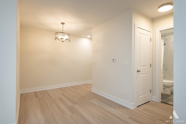 unfurnished room with light wood finished floors, a chandelier, and baseboards