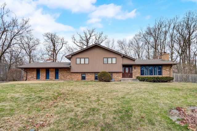 split level home with brick siding, a chimney, a front lawn, and fence