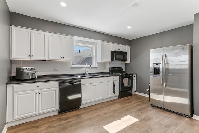 kitchen with light wood-style flooring, a sink, black appliances, white cabinets, and dark countertops