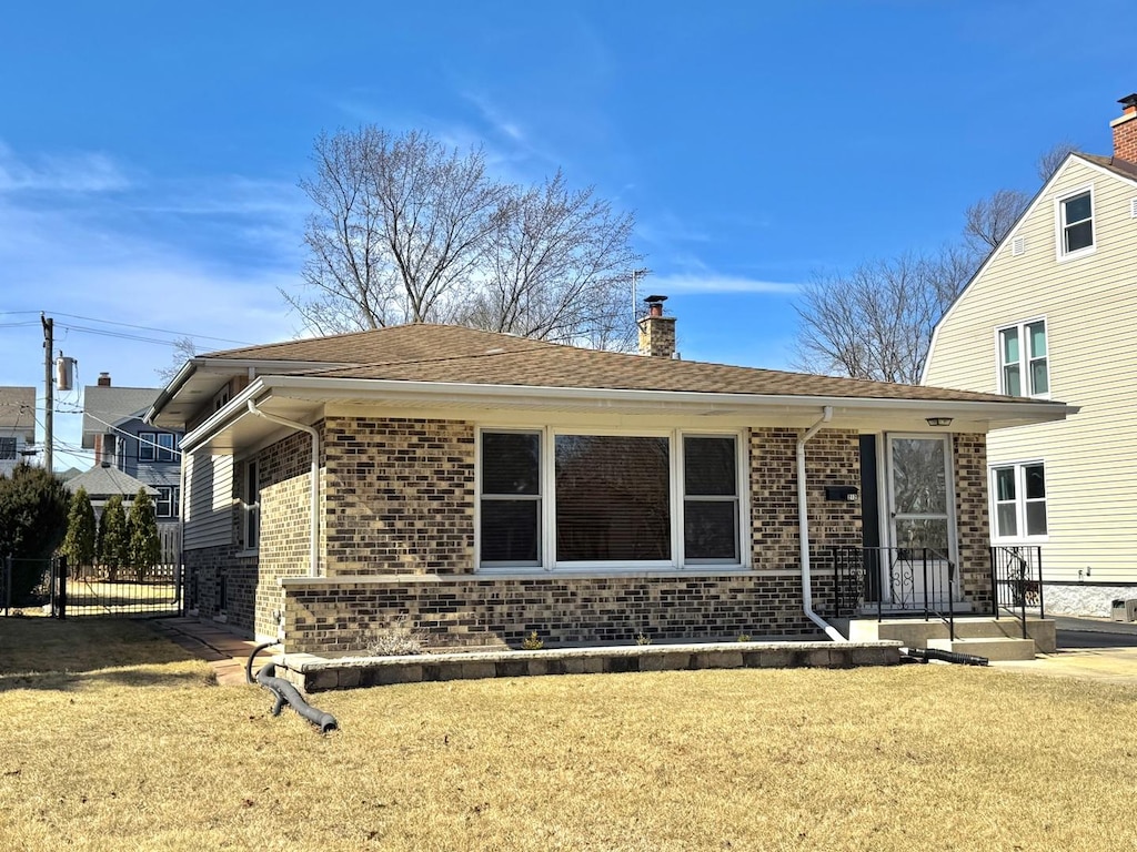 view of front of property with brick siding, a chimney, a front lawn, and fence