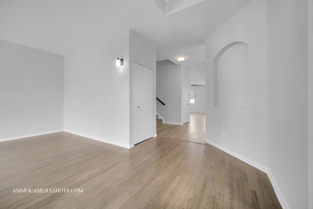 unfurnished room with arched walkways, stairway, light wood-style flooring, and baseboards