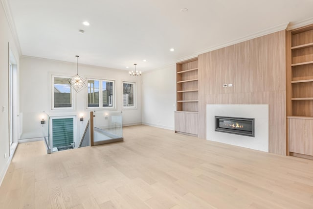 unfurnished living room featuring crown molding, built in features, an inviting chandelier, wood finished floors, and a glass covered fireplace