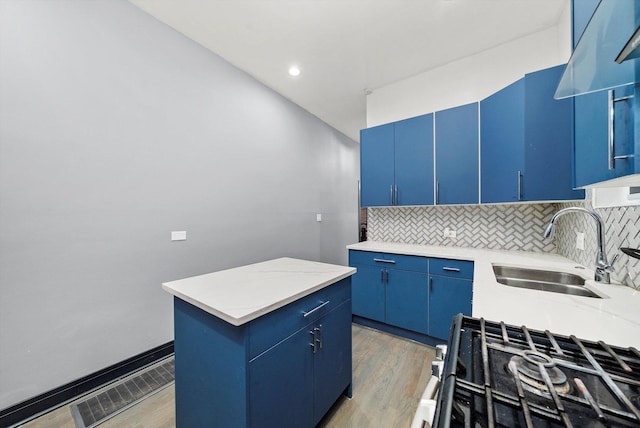 kitchen with blue cabinets, visible vents, a sink, light wood-style floors, and decorative backsplash