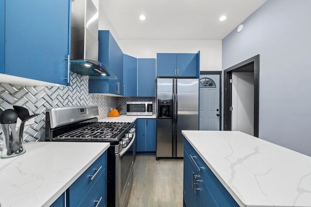 kitchen with blue cabinetry, tasteful backsplash, appliances with stainless steel finishes, and wall chimney exhaust hood