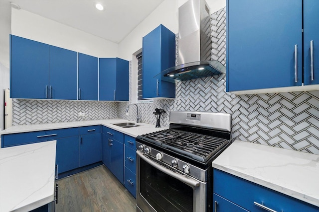 kitchen with stainless steel gas stove, blue cabinetry, wall chimney range hood, and a sink