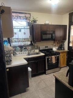 kitchen with stainless steel gas range, light tile patterned flooring, light countertops, dark brown cabinets, and black microwave