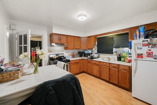 kitchen featuring under cabinet range hood, gas range, freestanding refrigerator, fridge, and a sink