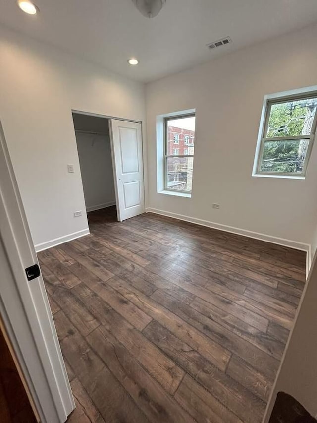 unfurnished bedroom with visible vents, multiple windows, and dark wood-type flooring