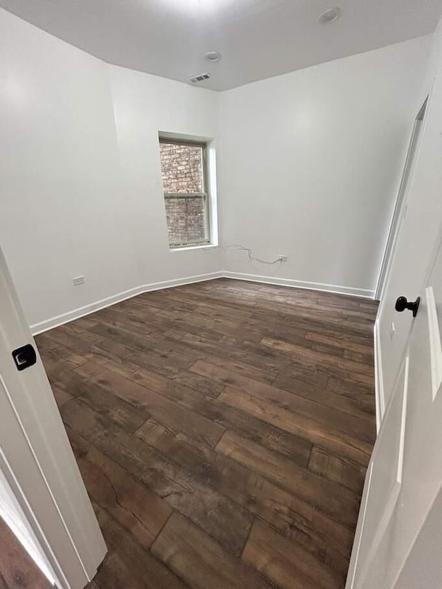 empty room featuring visible vents, dark wood-style floors, and baseboards