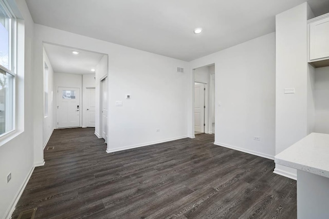 unfurnished living room featuring dark wood-style floors, baseboards, and a wealth of natural light