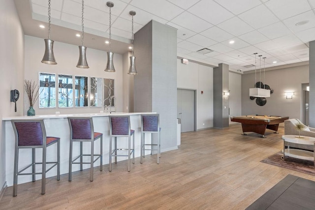 kitchen with pool table, decorative light fixtures, a breakfast bar, a high ceiling, and light wood-style floors