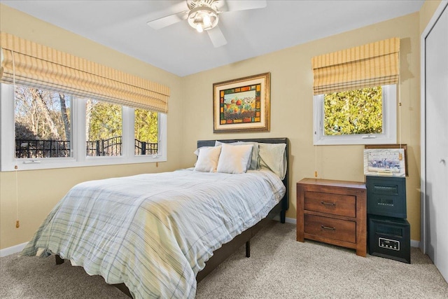 bedroom featuring baseboards, multiple windows, light colored carpet, and ceiling fan