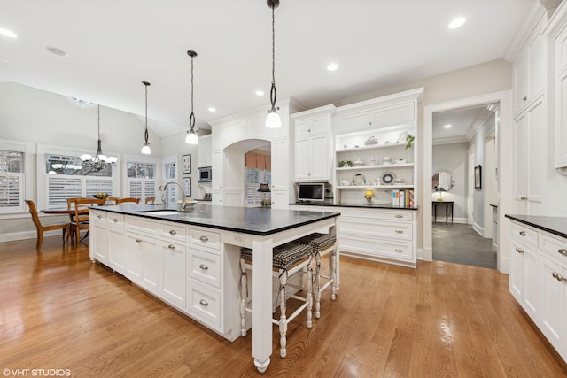 kitchen featuring dark countertops, open shelves, arched walkways, white cabinetry, and a sink