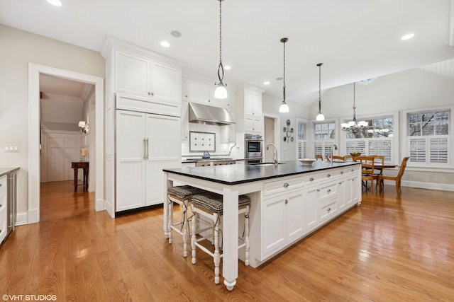 kitchen featuring dark countertops, under cabinet range hood, light wood-style flooring, white cabinets, and a sink