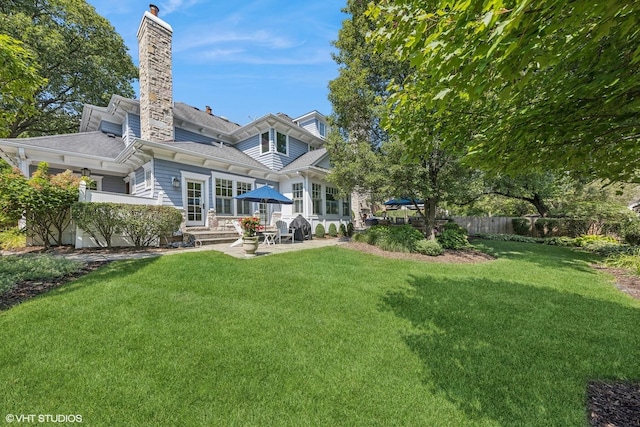 rear view of house with a patio area, a lawn, a chimney, and fence