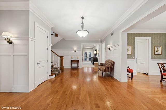 foyer with visible vents, wood finished floors, crown molding, a decorative wall, and stairs