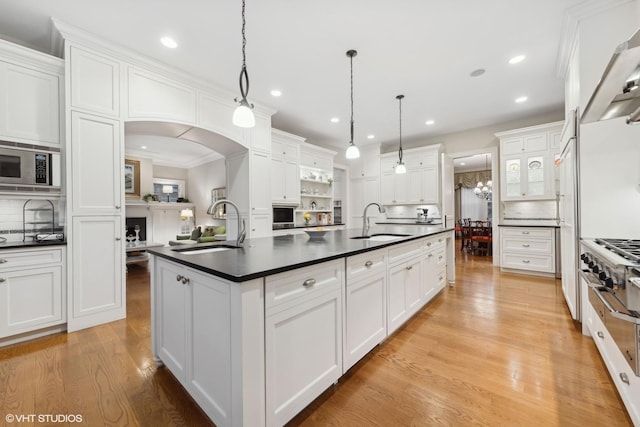 kitchen with a sink, dark countertops, a center island with sink, and ventilation hood