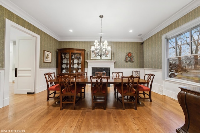 dining area with crown molding, an inviting chandelier, wainscoting, and wallpapered walls