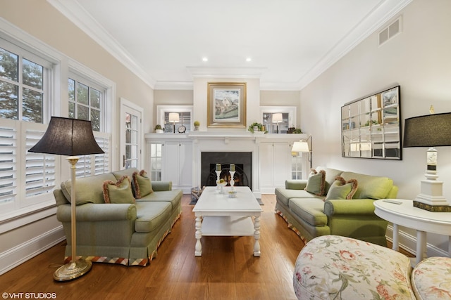 living area with visible vents, wood-type flooring, a fireplace, crown molding, and baseboards