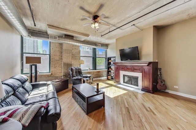 living room featuring baseboards, visible vents, a premium fireplace, light wood-style flooring, and ceiling fan