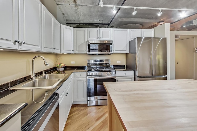 kitchen with a sink, rail lighting, appliances with stainless steel finishes, white cabinetry, and light wood-type flooring