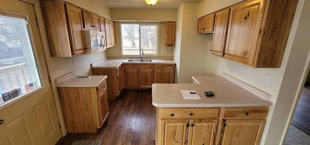 kitchen with a sink, dark wood-style floors, a peninsula, light countertops, and white microwave