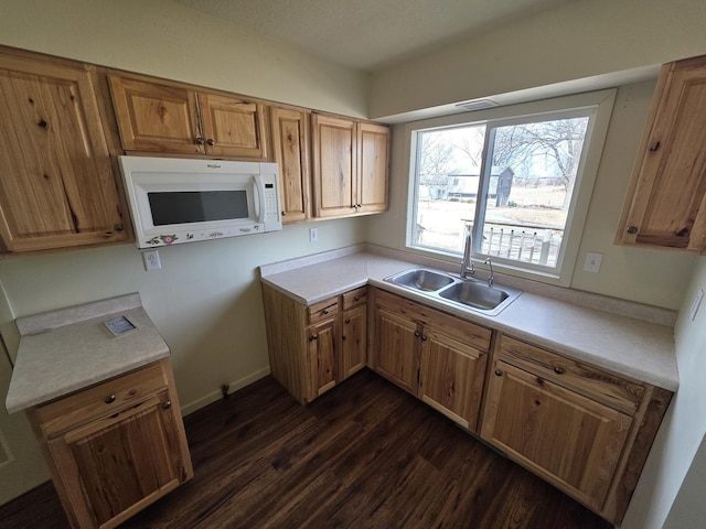 kitchen featuring brown cabinets, a sink, light countertops, white microwave, and dark wood-style flooring